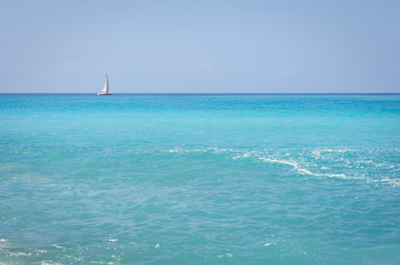 Fototapeta na wymiar Seascape. The coast of the Ligurian Sea, with turquoise water. Sailboat on the horizon.