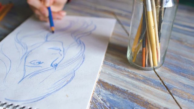 Young woman artist painting scetch on paper notebook with pencil closeup