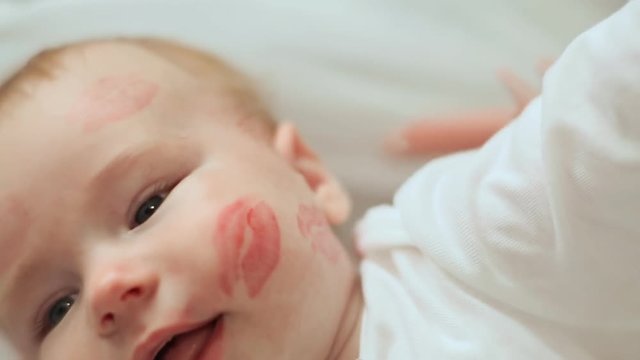 Mum kisses the baby and leave a bright trace of lipstick kiss. Slow motion shooting.