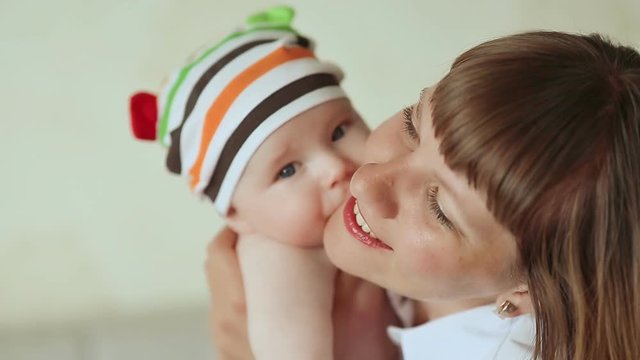 Baby tenderly kisses his mother. Dressed baby in striped shorts and cap