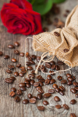 Roasted coffee beans, fresh red rose, coarse burlap sac on old wooden table. Rustic still life. Place for text. Top view. Concept romantic morning with your favorite