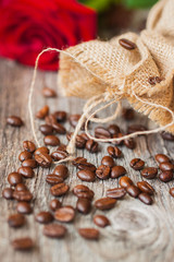 Roasted coffee beans on a brown wooden background, coarse roughly woven burlap and red rose, grunge texture. selective focus. Concept romantic morning with your favorite