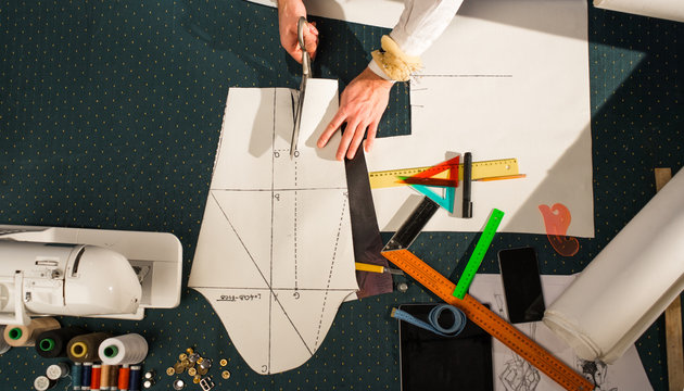 Tailor in the studio with scissors cuts the pattern sleeves