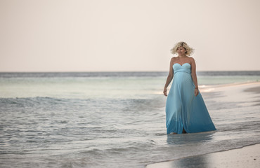 Fototapeta na wymiar Happy pregnant woman is walking on the Maldivian beach