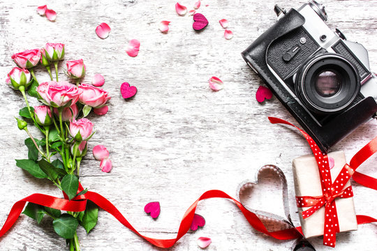 vintage retro camera with pink roses bouquet, red ribbon and gift box