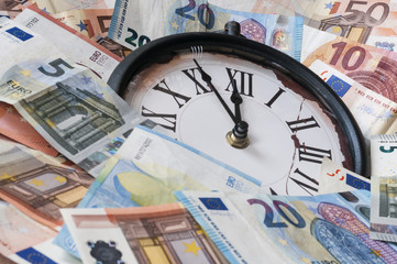 Fuenf Minuten vor zwoelf Uhr / Euro Geldscheine und eine Uhr, die Zeiger stehen fuenf Minuten vor zwoelf.