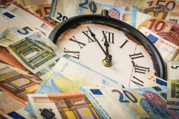Fuenf Minuten vor zwoelf Uhr / Euro Geldscheine und eine Uhr, die Zeiger stehen fuenf Minuten vor zwoelf.