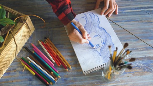 Young woman artist painting scetch on paper notebook with pencil closeup