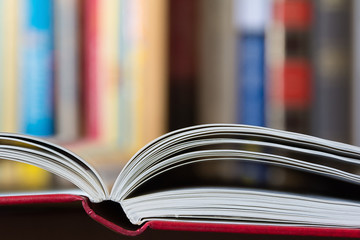 An open book in foreground with a blurred colorful library in background