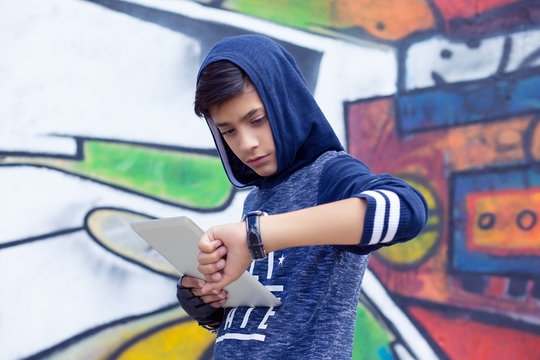 serious young man boy in blue hoody sweater checking syncing pad with smart watch