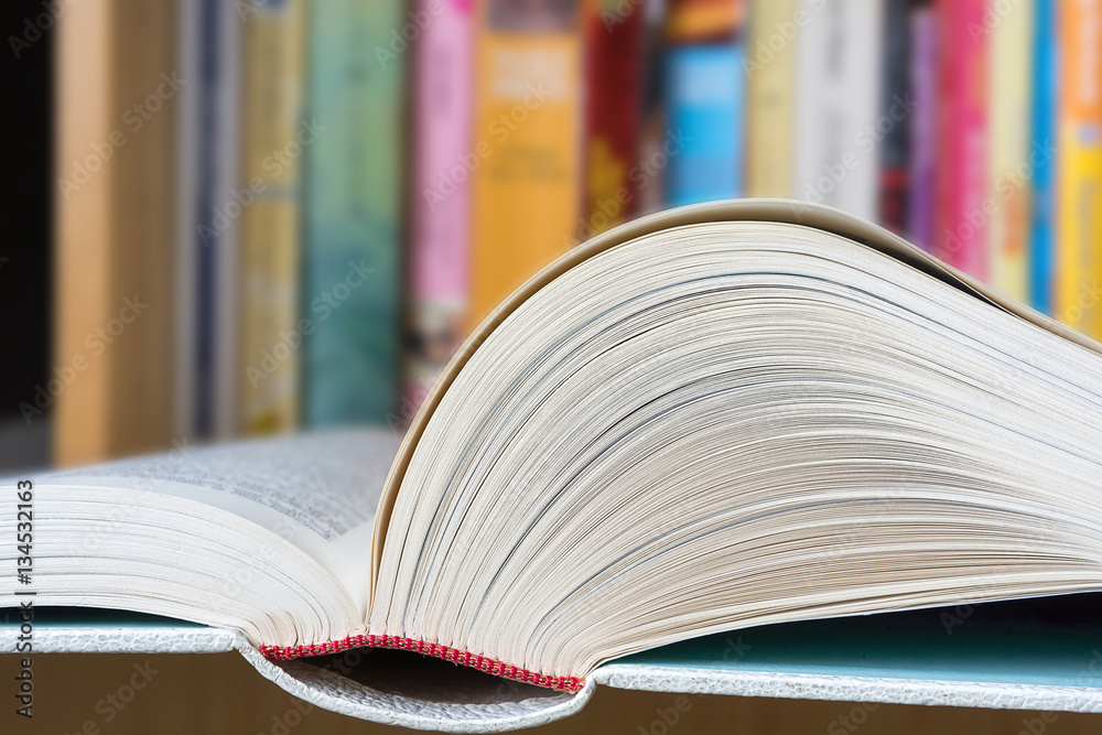 Wall mural an open book in foreground with a blurred colorful library in background