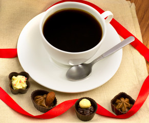white cup of coffee with chocolates and wood nuts on burlap clos