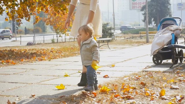 Cute baby boy walking with mother on path at autumn park