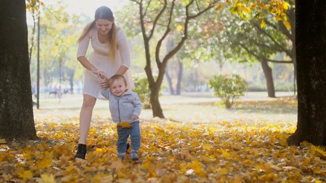 Slow motion footage of cheerful baby boy walking with mother on ground covered with autumn leaves