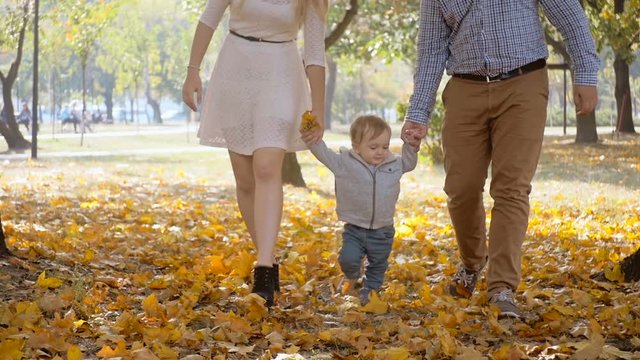 Slow motion footage young parents holding their baby son and walking at autumn park