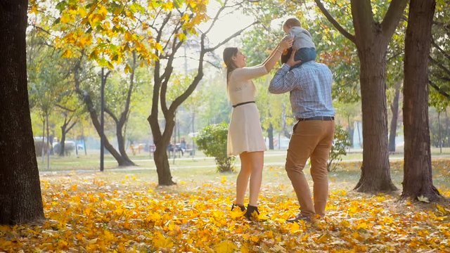 Slow motion footage of happy family walking with baby son sitting on fathers shoulders at autumn park