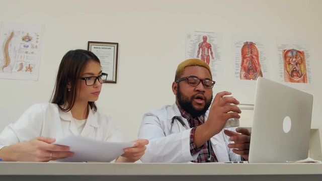 Two doctors showing pills to patient through webcam