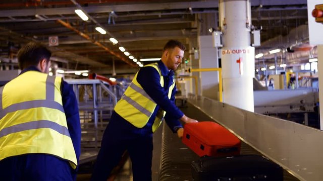 Two Airport Worker Putting Baggage On Baggage Carousel At Airport