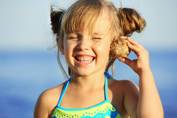 Obraz premium Cute girl listening to seashell at sea