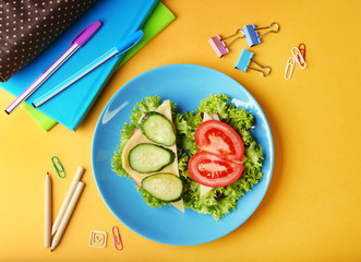 Blue plate with tasty sandwiches and stationery on yellow background