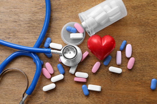 Red heart with stethoscope and pills on table