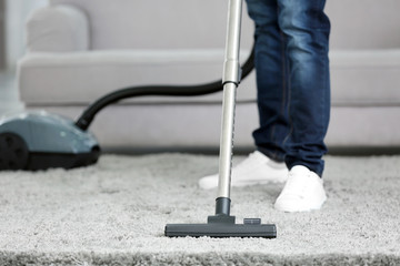 Closeup of man with vacuum cleaner cleaning carpet at home