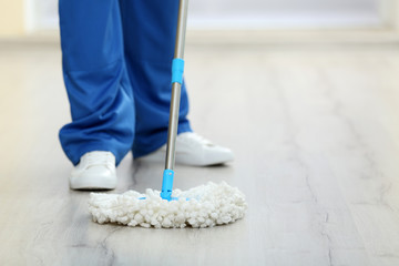 Young man with mop cleaning floor in the room, closeup