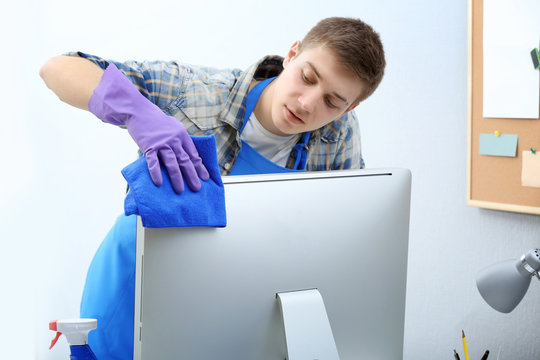 Young man cleaning computer monitor in office
