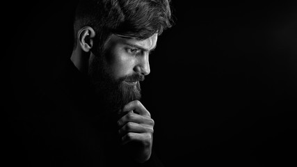 Puzzled young man touching beard looking down over black backgro
