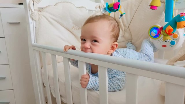 Adorable baby boy biting wooden crib while teething