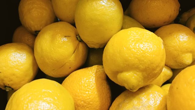 Closeup dolly shot of fresh yellow lemons lying on counter at grocery store
