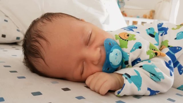 Portrait of cute newborn baby with soother sleeping in bed