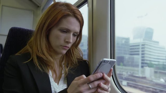 Commuter on her way to work looking out of the window and using smart phone