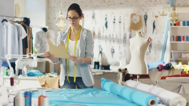 Beautiful Female Fashion Designer Straightens Roll of Teal Fabrics and Lays Out Templates on it. Shot in a Colorful Light Studio.  Shot on RED EPIC 4K (UHD).