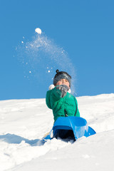 Boy playing in the snow. Sledding on a snowy hill. Winter games. Baby joy of snow. Throwing snowballs.