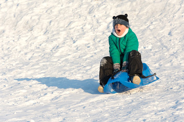 Fototapeta na wymiar Boy playing in the snow. Sledding on a snowy hill. Winter games. Baby joy of snow. Throwing snowballs.