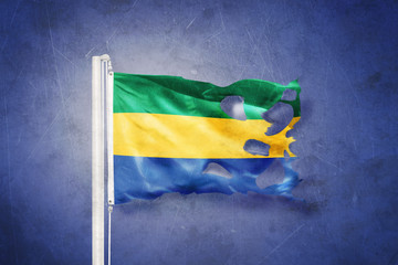 Torn flag of Gabon flying against grunge background