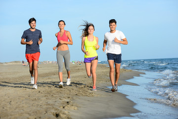 group of young people running in the sand on the shore of a beach by the sea at sunset during a sunny summer holiday vacation
