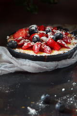 Delicious berry tart (tartlet) with cream on dark background