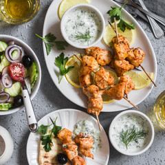 Greek lunch - chicken kebabs, greek salad, tzatziki, flatbreads and white wine. On a light background, top view