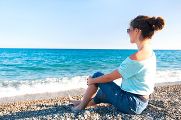 Fototapeta na wymiar Young beautiful teenage girl sitting on Mediterranean Sea pebble
