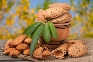 almonds with leaves in a bowl on the old wooden board  blurred garden background