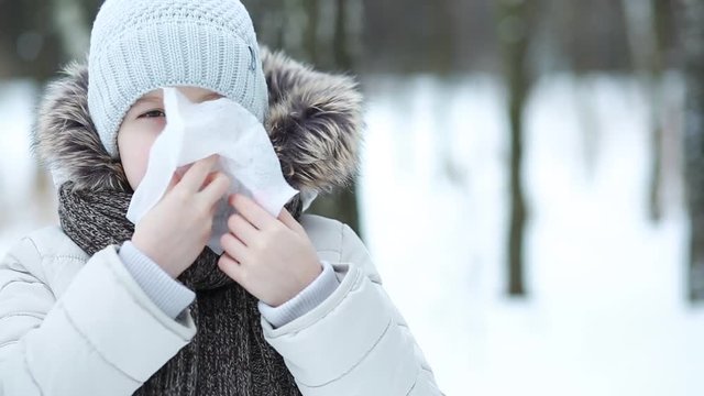Girl wipes her nose with a tissue in the winter park