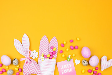 Easter decoration with eggs, bunny bag and candy on yellow background
