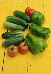 green peppers, cucumbers and tomatoes on a yellow wooden background