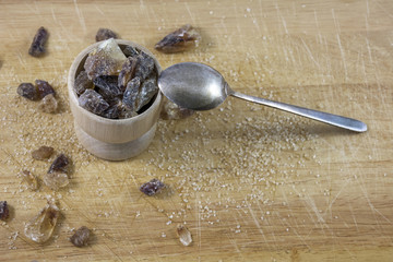 Brown sugar in wooden cup with teaspoon on wooden background