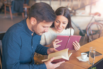 Young couple drinking coffee and reading a book in the cafe. Edu