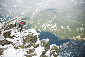 Fototapeta premium Hiker standing on a rock. Winter landscape. Shot of a young hiker taking photos from the top of a mountain