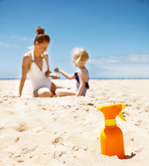 Closeup on sunscreen bottle on beach. Family in background