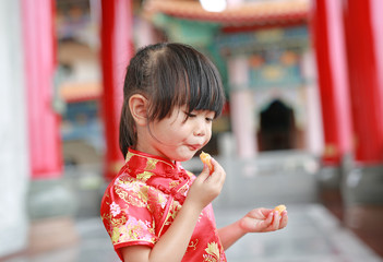 Cute asian kid girl in Traditional Chinese dress eating sacred orange fruit at chinese temple in bangkok thailand.